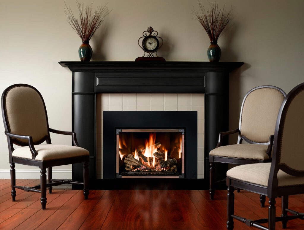 Classic-style living room with dark wood floors, three upholstered chairs, and a traditional black mantel framing a glowing gas fireplace.