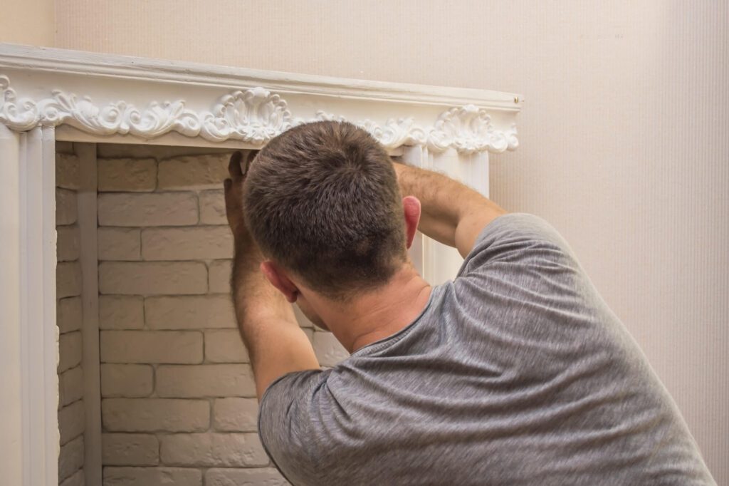 Worker performing fireplace maintenance, adjusting decorative molding on a white brick hearth surround.